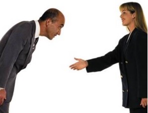 A stock photo of a man bowing and a woman holding out her hand for a handshake.