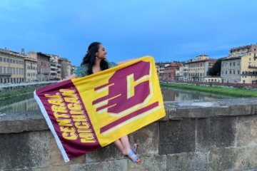 Student abroad holding Central Michigan University flag.