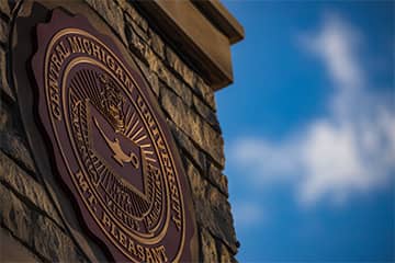 Central Michigan University's seal on a stone column with a blue sky in the background.