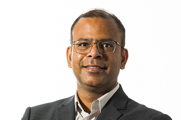 Professional photo of Dr. Sanjay Kumar, a man with dark hair wearing glasses, a dark suit coat and a light button up shirt.