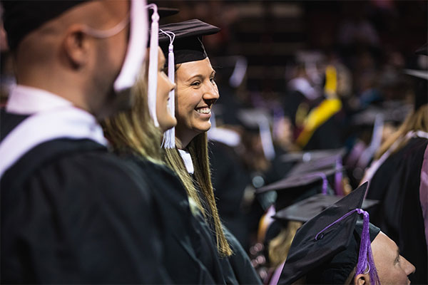 Students in their caps and gowns smile at commencement.