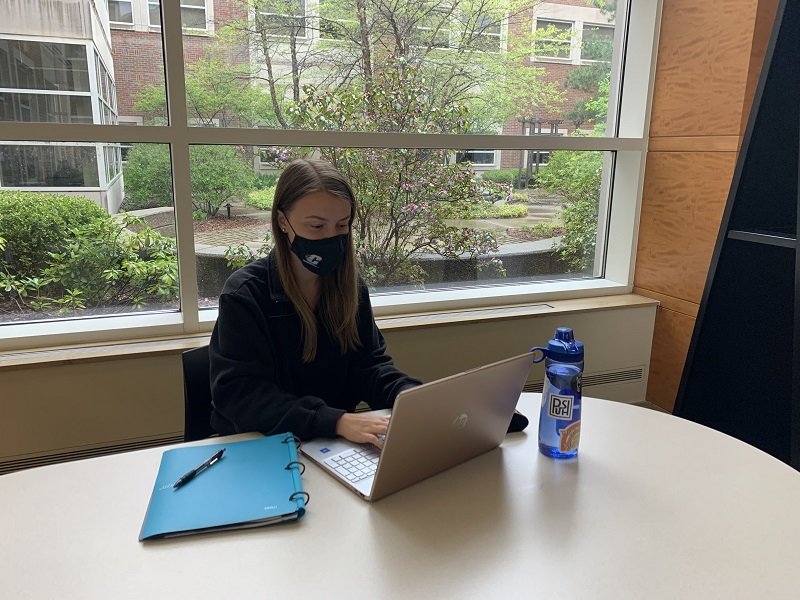 A student sitting at a table alone while working on a computer.