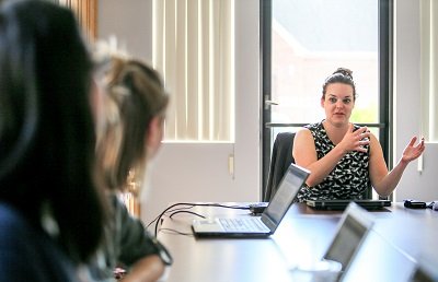 Three women sitting at a table with computers while talking with one another.