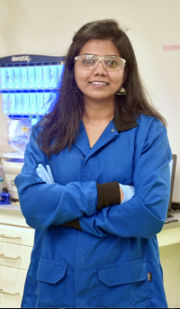 Dr. Sampa Maiti posing in a lab while wearing a lab coat and equipment
