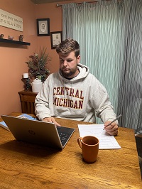 Bradley Madsen sitting at a table and working on a computer while taking notes.