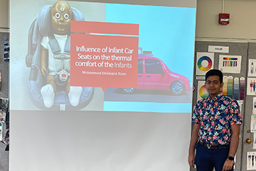 A student in a floral shirt standing in a classroom in front of a presentation on the Influence of Infant Car Seats on the thermal comfort of the Infants.