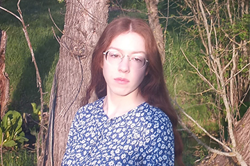 A woman in a blue floral shirt posing for a picture outside.