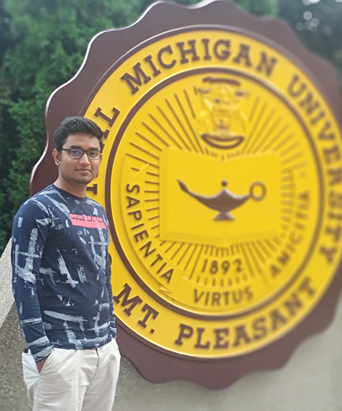 Ezazul Haque Sabuz poses in front of the CMU seal after completing a project studying the effect of thin film coating on 3D printed steel corrosion.