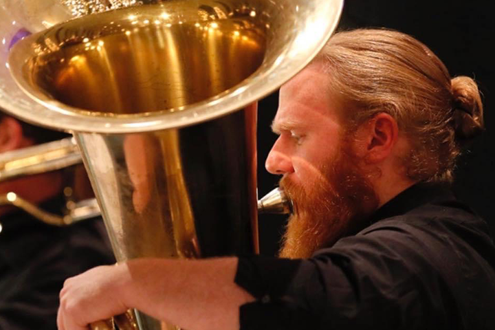 A man in a black collared shirt playing a tuba.