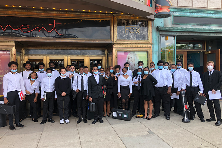 A large band wearing black & white posing for a picture in front of a theatre.