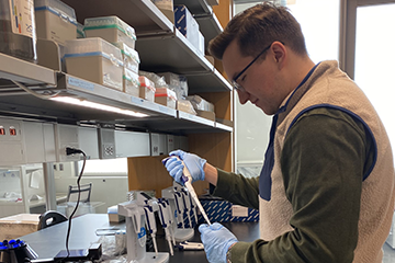 A man working in the biochemistry and molecular biology lab wearing a vest and glasses.