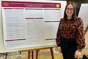 A woman in a leopard print blouse standing in front of a research presentation poster.