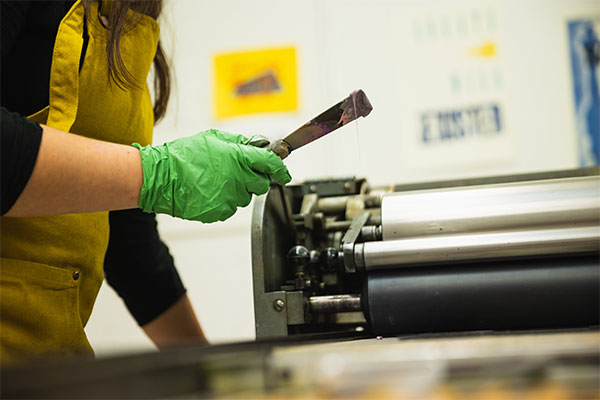 A student wearing an apron holds a putty knife during print making.