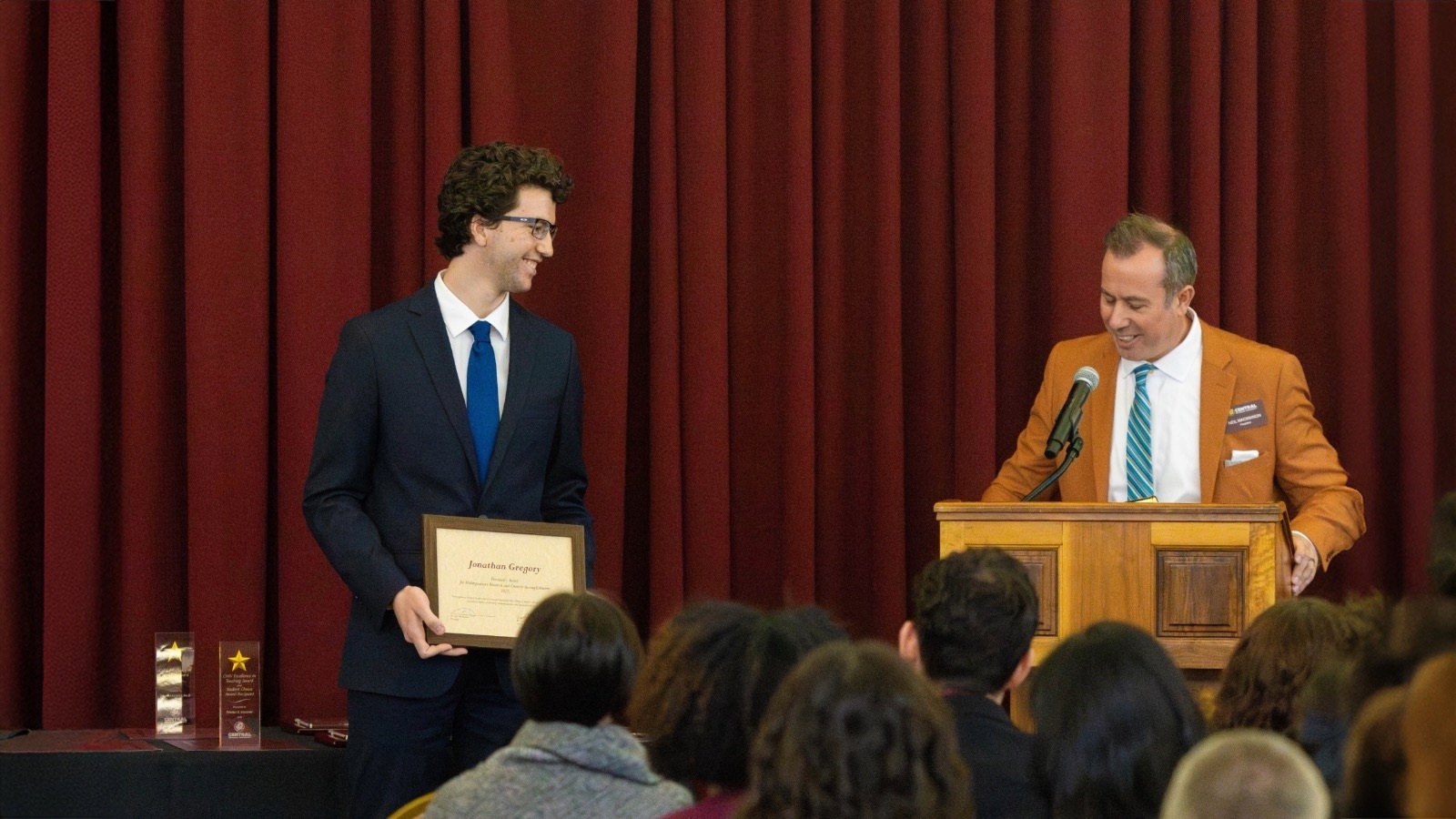 A man holding a certificate and smiling at another man.