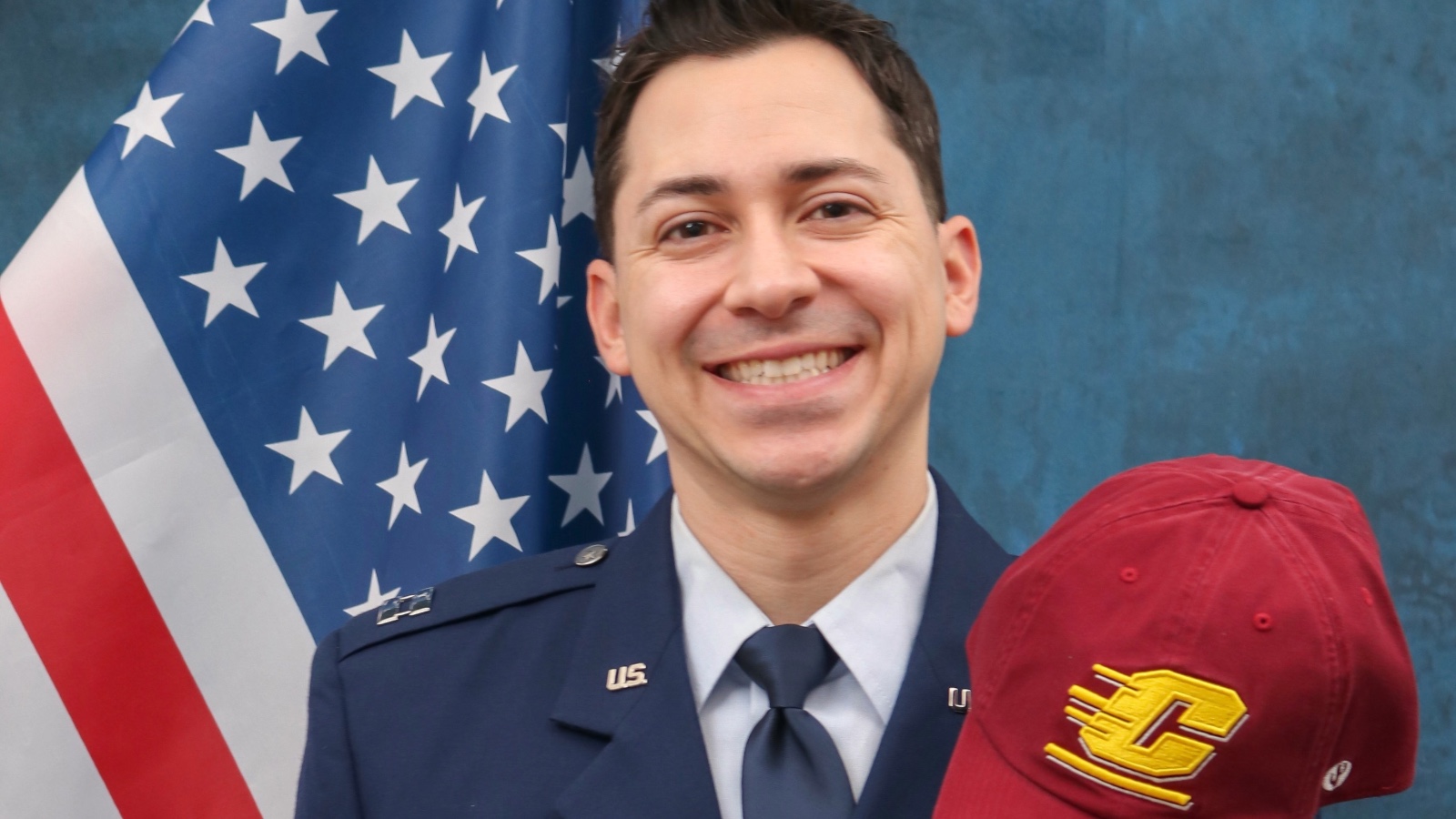 a man in uniform smiling in front of a flag