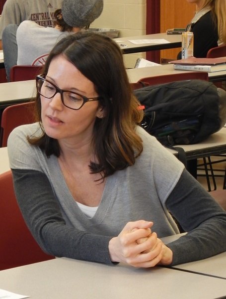 Dr. Carlin Borsheim-Black sitting at a desk in a classroom.