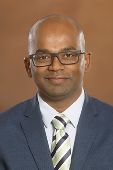 Professional headshot of Dr. Kumar Yelamarthi in a suit against a brown background.