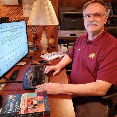 Dr. Mark Cwiek wears Central Michigan University apparel while sitting and working at a computer.