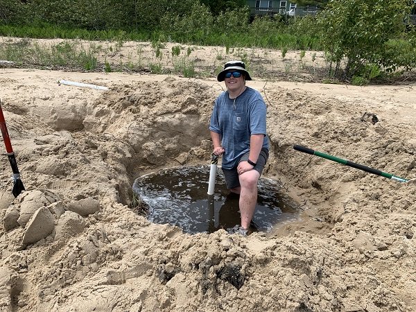 A person on a beach standing in a big puddle of water that is in the sand.