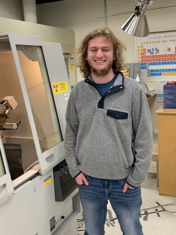 A student standing in a lab while smiling for the camera.