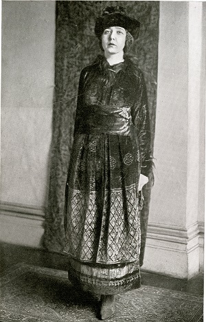 A black and white picture of a woman wearing a long dress and a hat.
