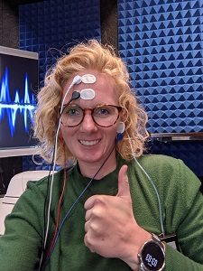 A woman wearing a green sweater with wires and sensors attached to her forehead and ears.
