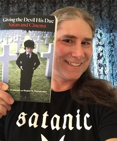 Dr. Jeffrey Weinstock holding his book, Giving The Devil His Due: Satan and Cinema, while smiling for the camera.