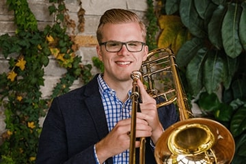 A man posing for a picture with his trombone.