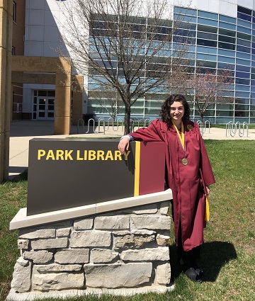 Undergraduate student, Nicole Polemitis, in her graduation gown next to Park Library sign