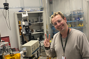 A man in a tan sweater posing for a picture in a lab.