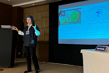A woman in a black outfit and blue cap presenting in front of a projector.