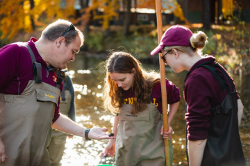 A picture of 3 people in CMU gear and waders looking at a mussel.