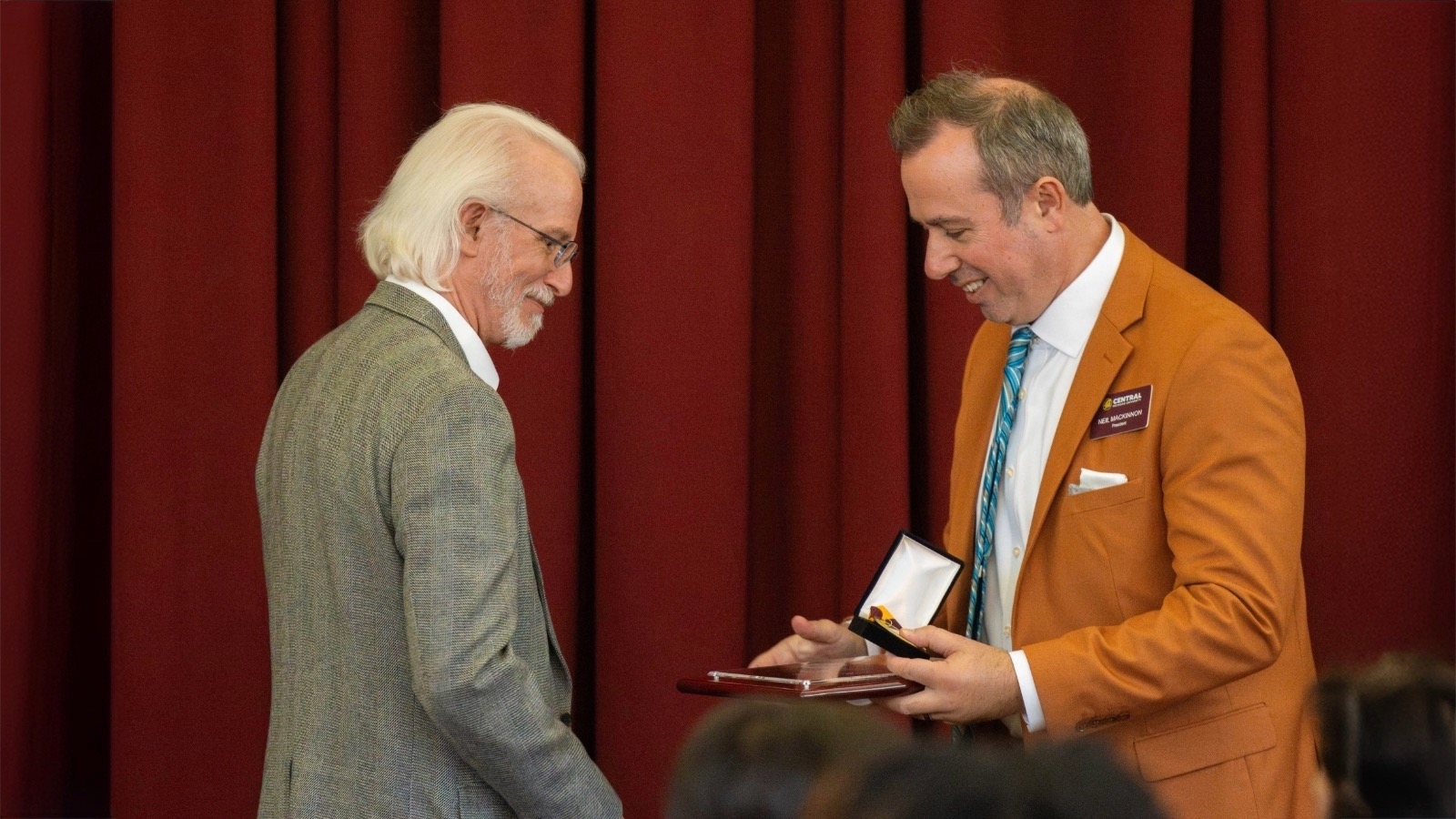 A man in a suit and tie giving another man an award.