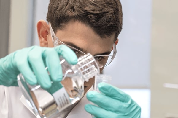 Chemistry student pouring solution into beaker.