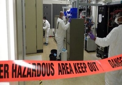 People in protective lab gear working in a taped off hazardous room.