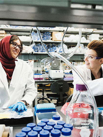Two female students in lab coats work in a sepsis lab on campus.