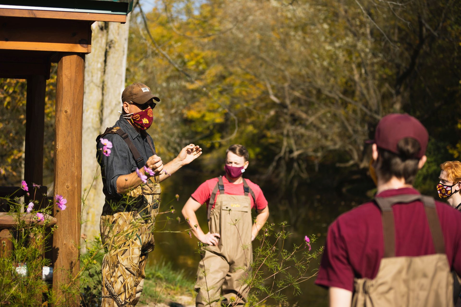 A group of people standing outside by a river while wearing masks and waders.