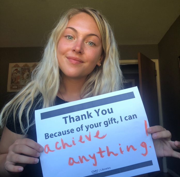 A student holding a piece of paper, thanking their scholarship donor for their gift.