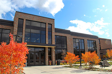 Exterior of Grawn Hall at Central Michigan University, featuring brick architecture, large windows and vibrant orange and red fall foliage.