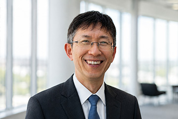 Portrait of accounting professor Keejae Hong smiling in a black suit and blue tie with a blurred office background.