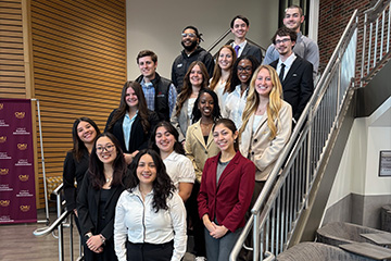 Queller Leadership Scholars pose together in new business clothes on a staircase inside the College of Business Administration.