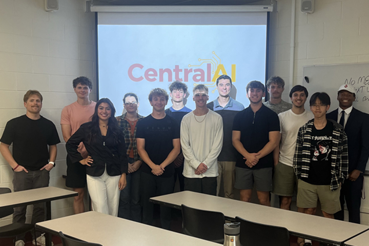 Thirteen business students stand in front of a projector screen that shows the Central AI logo. They are gathered for a regular RSO meeting on campus where they talk about AI in business.