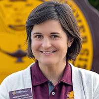 Alisha Draper smiling in a professional headshot, wearing a maroon polo and light cardigan with the CMU seal in the background.