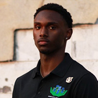 Carnell Poindexter in a professional headshot wearing a black Inner City Inclusion polo, standing outdoors against a neutral wall.