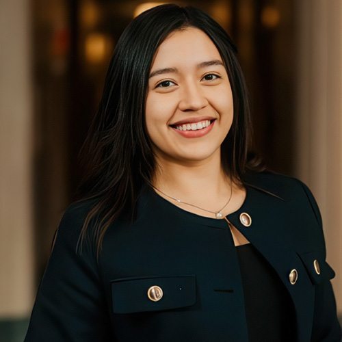 Carolina Hernandez Ruiz smiling in a professional headshot, wearing a dark blazer in a softly lit indoor setting.