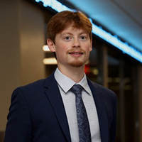 Cole Carpenter smiling in a professional headshot, wearing a suit and tie in an indoor setting.