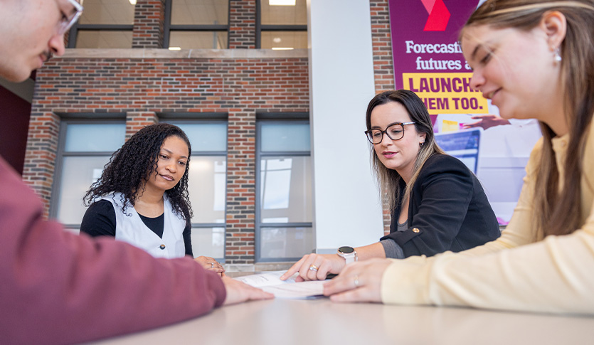 Students gather with a professor at a table in the atrium to review an assignment.