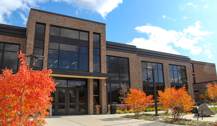 Exterior of Grawn Hall at Central Michigan University, featuring its brick facade, large windows and entrance framed by vibrant orange and red fall foliage.