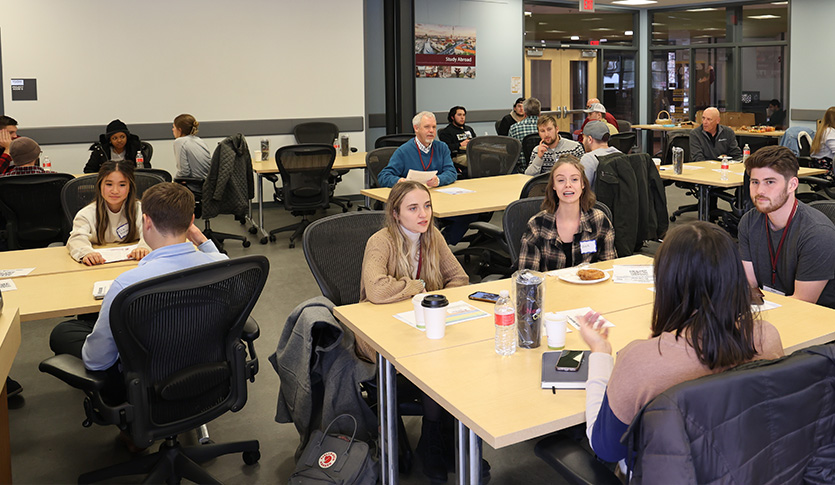 CMU students and other attendees sit in small groups around tables, talking and sharing ideas in a collaborative meeting space.