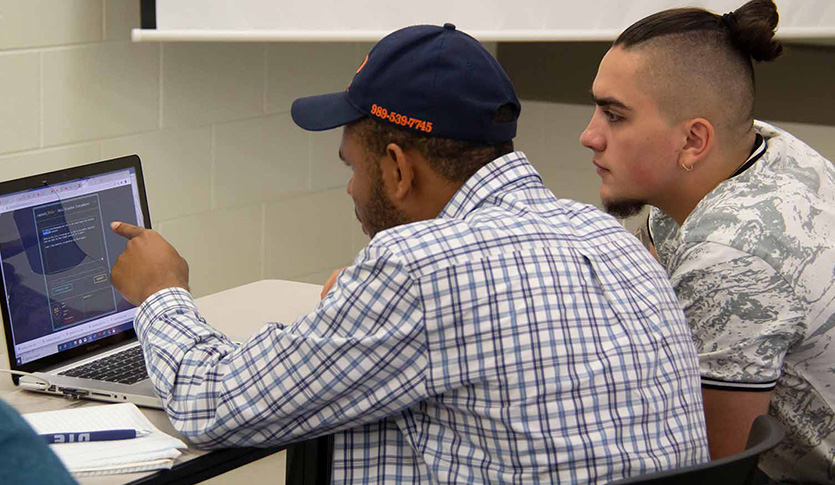 Students huddle over a laptop during a cybersecurity capture the flag game during the 2024 Cybersecurity Conference.